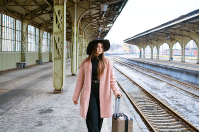 Young woman in coat walks with suitcase along empty platform of railway