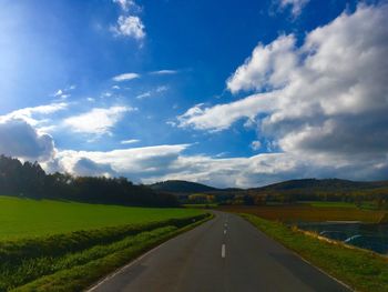 Empty road amidst field against sky