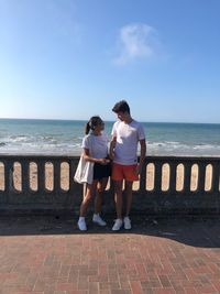 Couple standing by railing against sea 