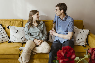 Mature man talking with teenage daughter while sitting on sofa at home