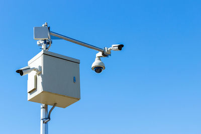 Low angle view of security camera against clear blue sky