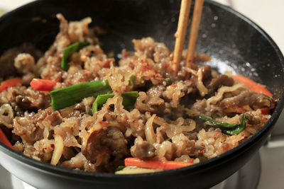 Cooking japanese sliced beef with green onion, carrot, and onion slice using chopstick, close up