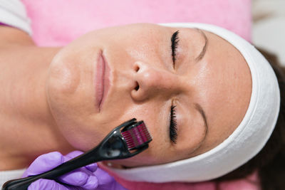 Close-up of woman lying down with while beautician using cosmetic roller on face at spa