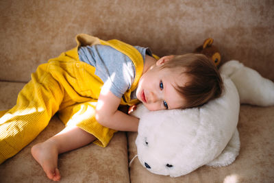 Funny little child is having fun, playing with soft toys on the couch at home.