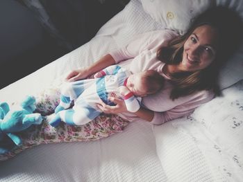 High angle portrait of smiling woman relaxing with baby boy on bed at home
