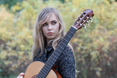 Beautiful young woman holding guitar outdoors