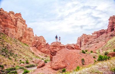 Low angle view of people standing on cliff against sky