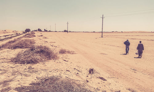 People walking on sand dune against clear sky