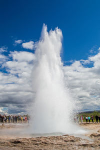 People looking at geyser against sky