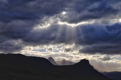 Low angle view of storm clouds over silhouette mountains