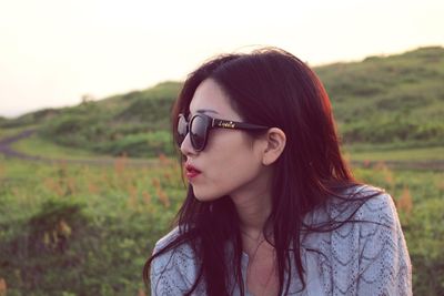 Close-up portrait of young woman with sunglasses against sky