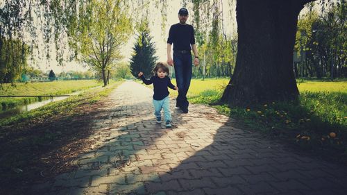 Full length of man walking with daughter on footpath at park