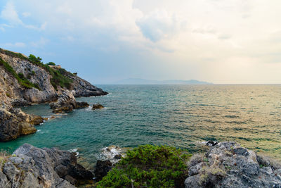 Scenic view of rock formation in sea against cloudy sky