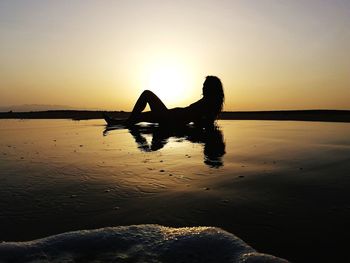 Silhouette relaxing on beach against clear sky during sunset