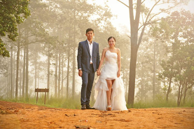 Full length portrait of bride and bridegroom standing on field