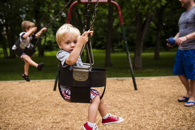 Low section of father with children enjoying swing in playground