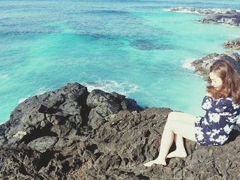 Full length of young woman relaxing on rock formation by sea during sunny day