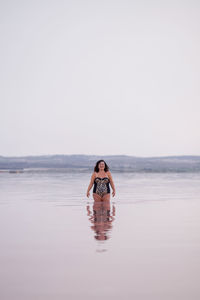 Delighted curvy female in bikini standing in water of pink pond in summer and looking at camera