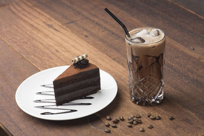 High angle view of chocolate cake in plate by iced coffee on table