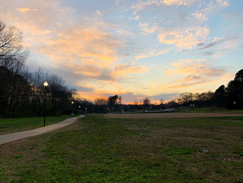 Road by trees against sky during sunset