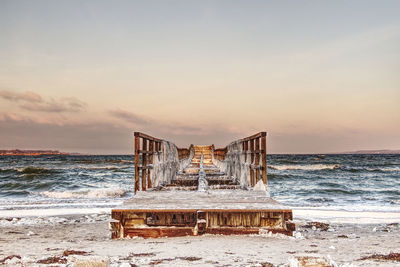 Pier at beach against sky during sunset