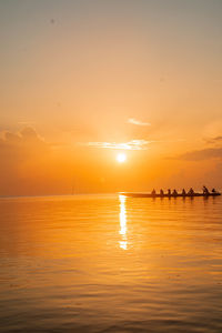 Silhouette people on beach against orange sky