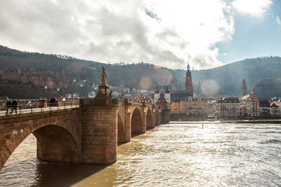 Arch bridge over river in city against sky