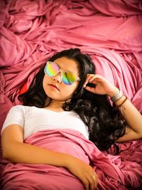 High angle portrait of woman in sunglasses sleeping on bed