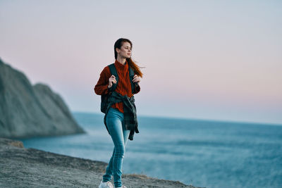 Young woman standing at beach against sky