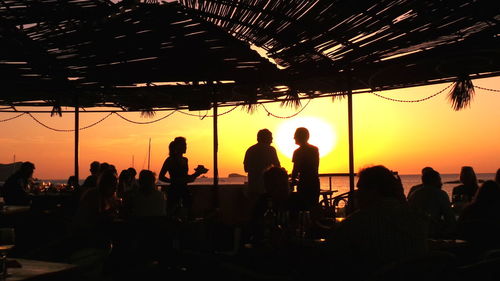 Silhouette people at beach restaurant during sunset