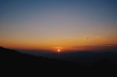 Scenic view of silhouette mountains against orange sky