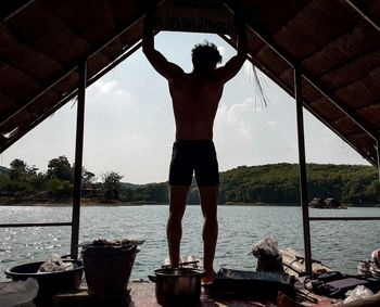 Rear view of shirtless man standing by lake