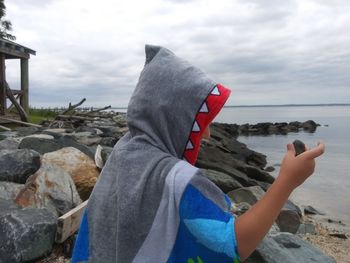 Midsection of woman on rock at beach against sky
