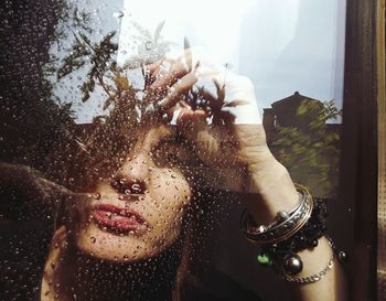 Close-up portrait of woman seen through wet glass window