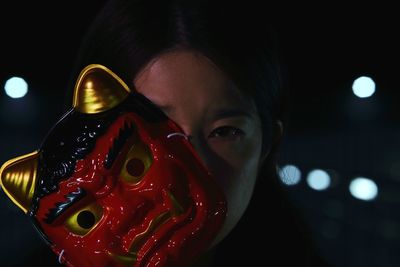 Close-up portrait of woman with mask standing in city at night