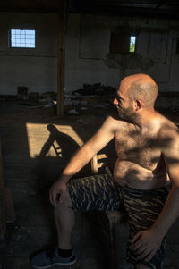 A model man sits in the dark space of an abandoned warehouse. his shadow is on the floor. 