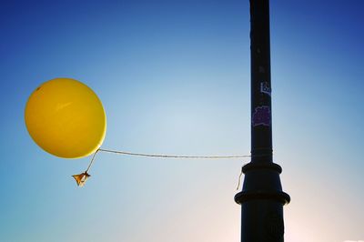 Low angle view of yellow balloon tied with pole against blue sky