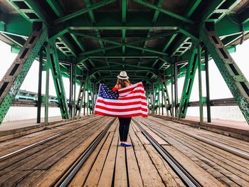 Woman holding american flag while standing on bridge