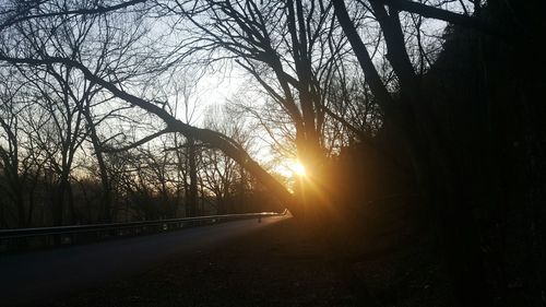 Silhouette bare trees by road against sky during sunset