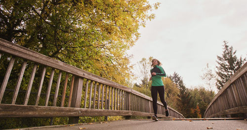 Woman standing on footbridge against trees