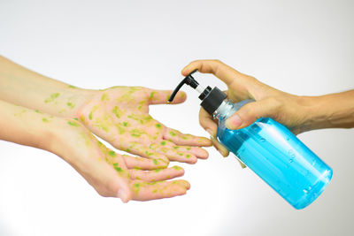 Close-up of hand holding bottle against white background