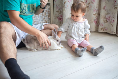 Low section of father with baby and rabbit at home