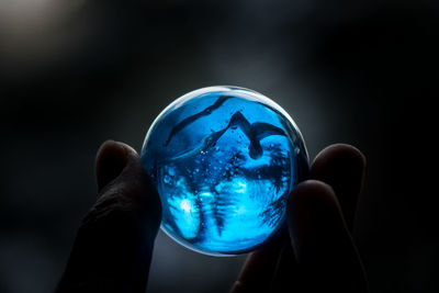 Close-up of hand holding crystal ball against black background