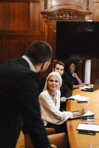 Colleagues looking at businessman discussing during meeting in board room