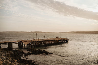 Wooden posts on beach against sky during sunset