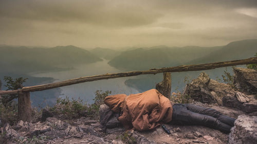 Horse relaxing on rock against sky