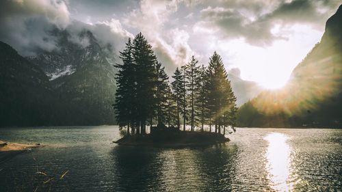 Scenic view of trees amidst lake against mountains and cloudy sky