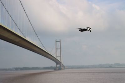 Low angle view of drone flying over bridge against sky