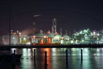 Illuminated factory by river against sky at night