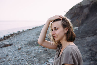 Beautiful relaxed young woman sits on a stone near the sea.